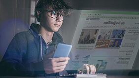 Ein Bub liest parallel auf Smartphone und Notebook